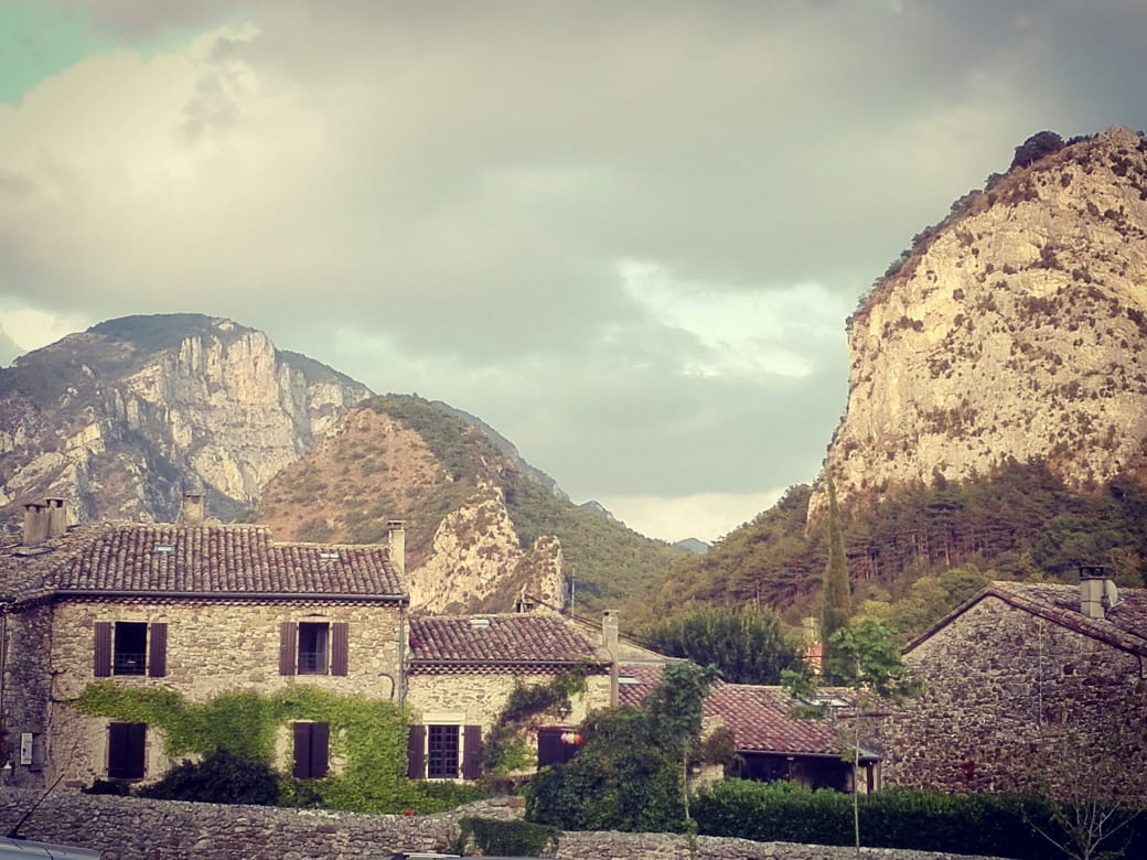 Paisaje del valle de la drome, con montañas, fondo de nubes, y casa antigua de piedra.